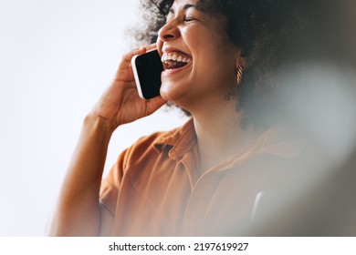 Businesswoman Laughing Happily While Speaking On A Phone Call. Cheerful Female Entrepreneur Communicating With Her Business Partners While Working In A Modern Office.