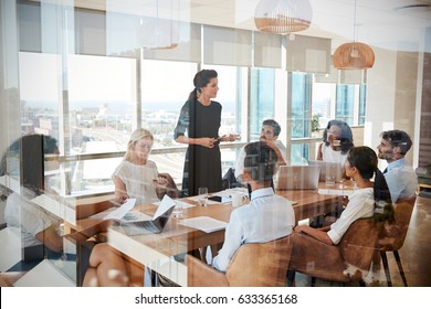 Businesswoman Leads Meeting Around Table Shot Through Door