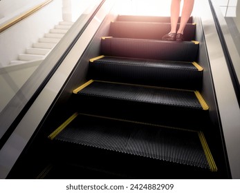 Businesswoman legs wearing leather casual cut shoes standing on the escalator going up to outdoors with the warm sunlight. Way to success, business background concept. - Powered by Shutterstock