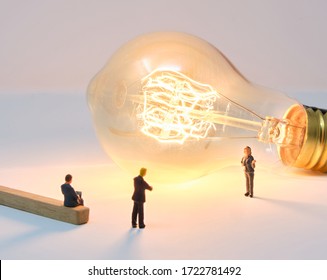 A businesswoman is lit by a large filament lightbulb (idea) as she presents to colleagues - Tiny People Working From Home - Powered by Shutterstock