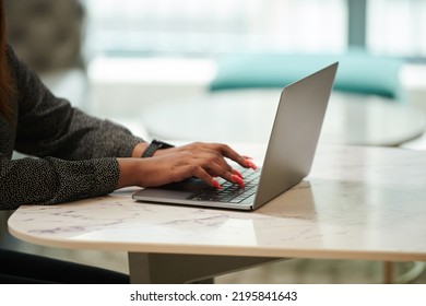 Businesswoman With Long Vibrant Nails Working On Laptop At Table In Her Tiny Apartment