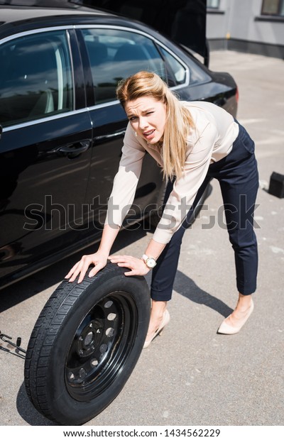 businesswoman looking at camera,\
rolling new wheel and fixing broken auto, car insurance\
concept