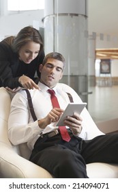 Businesswoman Looking Over Male Colleagues Shoulder Pointing At Digital Tablet