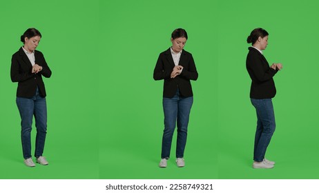 Businesswoman looking at wristwatch to check time over greenscreen backdrop, running late and waiting. Impatient corporate worker standing over isolated green screen background in studio. - Powered by Shutterstock