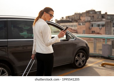 Businesswoman with luggage walking to the car on parking. Young woman going to business trip. - Powered by Shutterstock