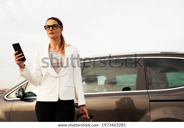 Businesswoman with luggage walking to
the car on parking. Young woman Going to business
trip.	