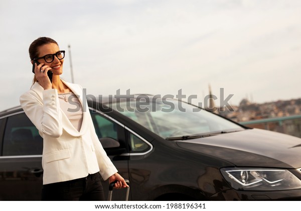 Businesswoman with luggage walking to\
the car on parking. Young woman Going to business\
trip..	