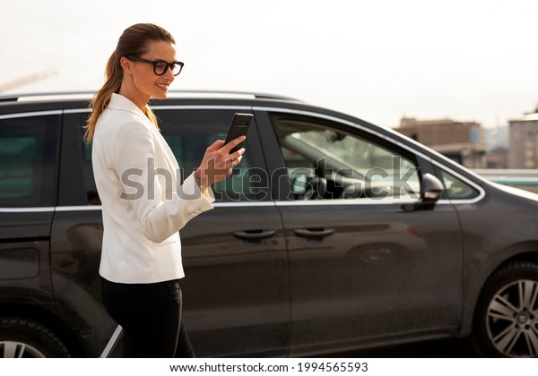 Businesswoman with luggage walking to the\
car on parking. Young woman going to business\
trip.