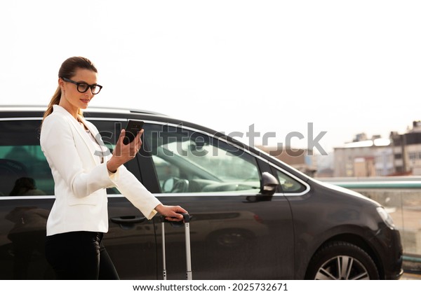 Businesswoman with luggage walking to the\
car on parking. Young woman going to business\
trip