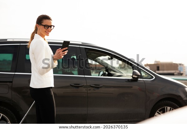 Businesswoman with luggage walking to the\
car on parking. Young woman going to business\
trip