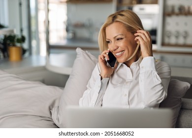 Businesswoman making a call while working on laptop on the bed