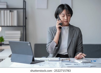 Businesswoman is making a phone call while analyzing financial charts and using a calculator in her office - Powered by Shutterstock