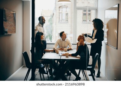 Businesswoman making a presentation to a diverse group of colleagues seated around and table inside of an office meeting room