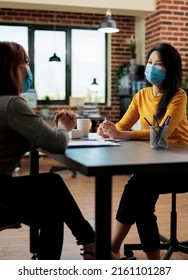 Businesswoman With Medical Face Mask Against Covid19 Discussing Business Partnership With Entrepreneur Woman Working At Management Project In Startup Office. Executive Managers Collaborating Together