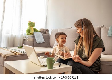 Businesswoman Mother Woman With A Toddler Working At The Computer. Working Mother Concept. Young Woman Working On Laptop With Her Child From Home. Stay At Home Mom Working Remotely On Laptop