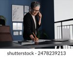 Businesswoman multitasking with paperwork and phone calls, demonstrating efficiency and professionalism in a corporate office.