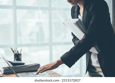 Businesswoman Navigating a Mountain of Work: A professional woman expertly navigates a cluttered desk, her focused gaze directed at a laptop amidst a towering stack of paperwork, showcasing the demand - Powered by Shutterstock