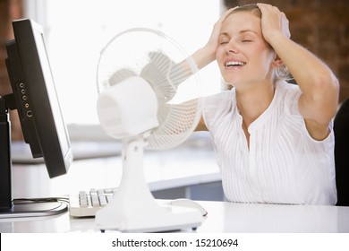 Businesswoman In Office With Computer And Fan Cooling Off