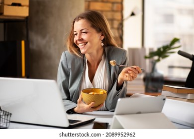 Businesswoman In Office Having Healthy Snack. Young Woman Eating Fruit While Having A Video Call	