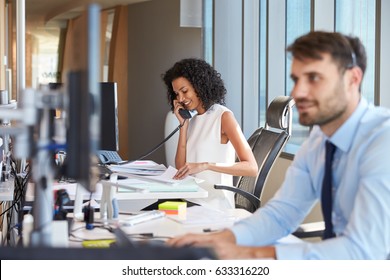 Businesswoman On Phone At Desk In Busy Office