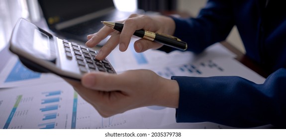 Businesswoman On Suit Hand Holding Pen And Press Calculator Button On The Desk With Paperwork At Workplace Office. Banner-wide Background.