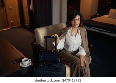 Businesswoman with packed suitcase sitting on armchair in hotel room - Powered by Shutterstock