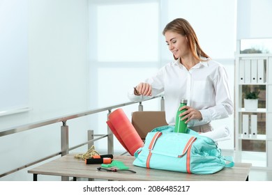 Businesswoman Packing Sports Stuff For Training Into Bag In Office