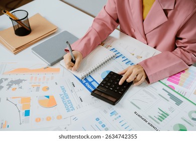 Businesswoman in pink suit is analyzing financial charts and calculating company expenses.