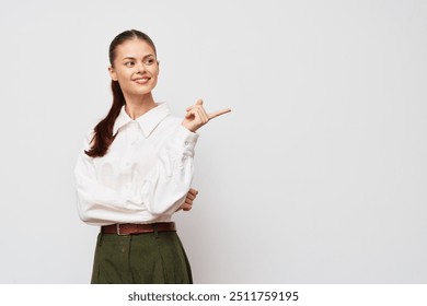 Businesswoman pointing gesture, smiling, dressed in a white blouse and green pants, on a light gray background, ideal for presentations or promotional materials - Powered by Shutterstock