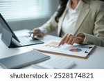 Businesswoman is pointing at a graph chart on a clipboard and working on a business project at her office desk