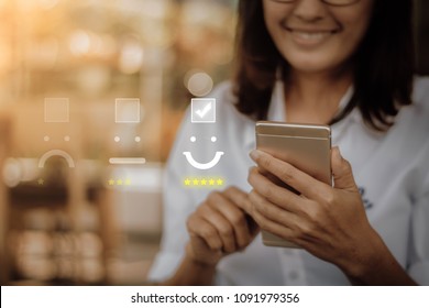 Businesswoman pressing face emoticon on virtual touch screen at smartphone .Customer service evaluation concept. - Shutterstock ID 1091979356