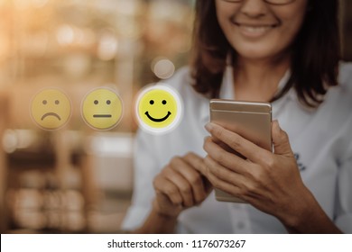 Businesswoman pressing face emoticon on virtual touch screen at smartphone .Customer service evaluation concept. - Shutterstock ID 1176073267