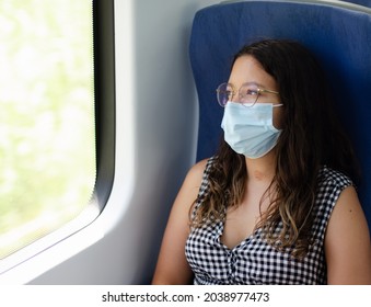 Businesswoman With Protective Face Mask And Glasses Looking Out Of The Window Of Train In Thought. Young Woman Thinking While Traveling By Train