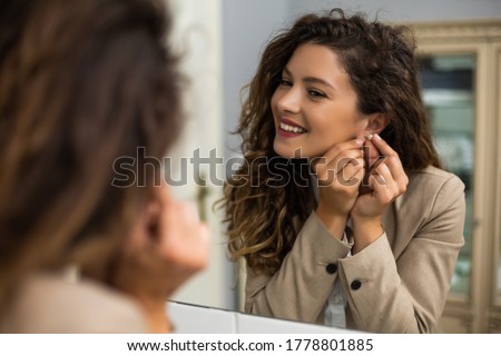 Businesswoman is  putting earrings while preparing for work.