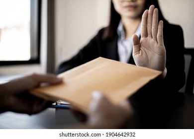 Businesswoman raised her hand to deny accepting a bribe from a business partner, a brown envelope containing a large number of dollar bills as money for bribery, a corruption concept. - Shutterstock ID 1904642932