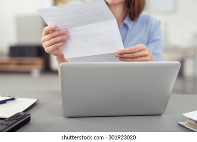 Businesswoman reading a handheld letter or document as she sits at her desk in the office in front of a laptop computer - Shutterstock ID 301923020