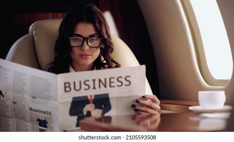 Businesswoman reading news near cup of coffee on table in private plane