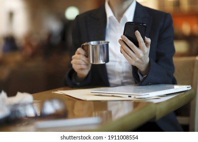 Businesswoman reading news on smartphone and drinking coffee in cafe
 - Shutterstock ID 1911008554