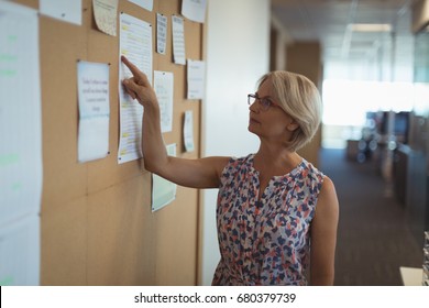 Businesswoman Reading Paper On Notice Board While Standing In Office