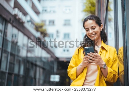 A  businesswoman reading something funny on her mobile phone on the street while going back home from work. Connected city worker. Close up of a young lady using a phone while on the street