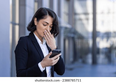 Businesswoman received notification message with bad news, woman reading online on phone, upset and confused sad using smartphone app, outside office building, walking in business suit. - Powered by Shutterstock