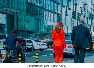 Businesswoman in a red suit and businessman walking along the modern city to work in the office. Office worker on a motorcycle - Powered by Shutterstock