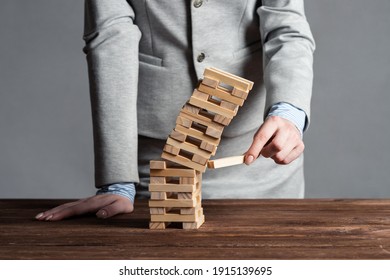 Empresaria quitando el bloque de madera de la torre que cae sobre la mesa. Gestión de riesgos e inestabilidad económica con juego de cubos de madera. Fracaso y colapso de las empresas