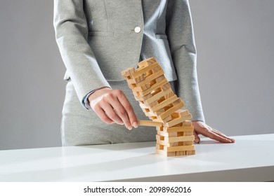 Businesswoman removing wooden block from falling tower on table. Management of risks and economic instability concept with wooden jenga game. Failure and collapse in corporate business - Shutterstock ID 2098962016