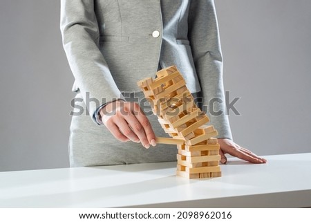 Businesswoman removing wooden block from falling tower on table. Management of risks and economic instability concept with wooden jenga game. Failure and collapse in corporate business
