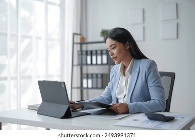 Businesswoman is reviewing documents and working with a digital tablet at her desk in the office - Powered by Shutterstock