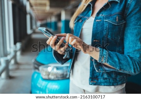 Businesswoman sending a message with a smartphone. A young proud businesswoman is talking on her mobile phone with a client and reading order. Woman standing nearby car texting message on a smartphone
