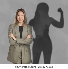Businesswoman and shadow of strong muscular lady behind her on grey wall. Concept of inner strength