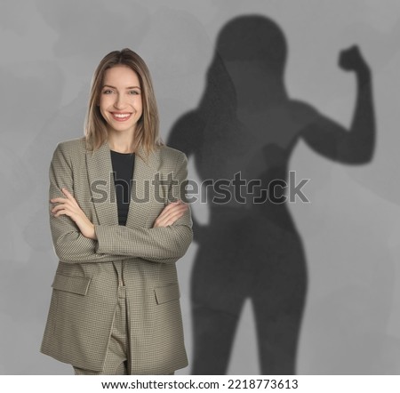 Businesswoman and shadow of strong muscular lady behind her on grey wall. Concept of inner strength