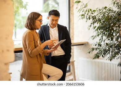 Businesswoman showing something on digital tablet to asian businessman in cafe or restaurant. Concept of remote and freelance work. Young caucasian girl wearing glasses. Idea of business cooperation - Powered by Shutterstock